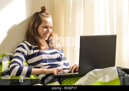 Junges Mädchen lernt zu Hause, mit Laptop im Bett Stockfoto