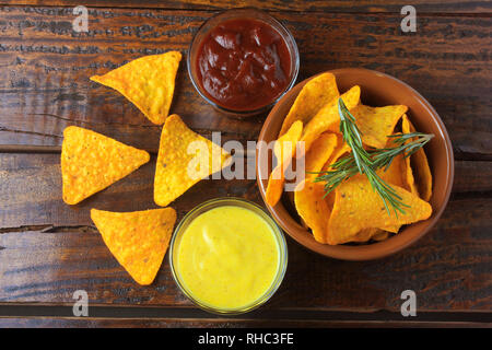 Nachos mais Chips in Keramik Schüssel auf hölzernen Tisch neben verschiedenen Soßen Stockfoto