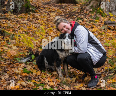 Eine junge Frau, die im Herbst mit ihrem Hund beim Wandern im Algonquin Park pausiert, um sich zu kuscheln Stockfoto