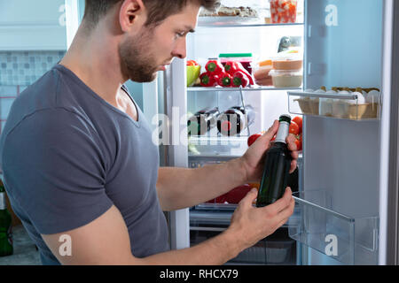 Junger Mann mit Bierflasche Stand vor der Kühlschrank Stockfoto