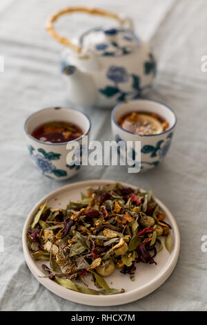 Kräutertee in einem weißen Keramik Platte mit Tee in Tassen und Teekanne verschwommen in der Ferne sehen. Selektive konzentrieren. Stockfoto