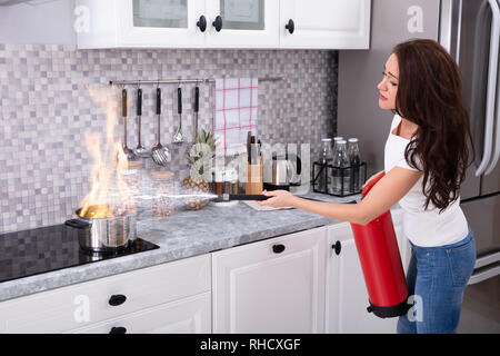 Frau mit Feuerlöscher zu stoppen Feuer zum Brennen von kochenden Topf in der Küche Stockfoto