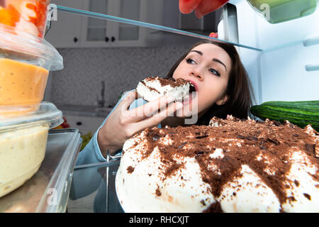 Junge Frau essen Kuchen aus dem Kühlschrank Stockfoto