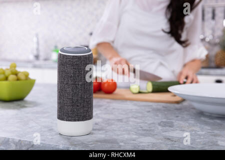 Close-up Voice Assistant Redner vor Frau Schneiden von Gemüse in der Küche Stockfoto