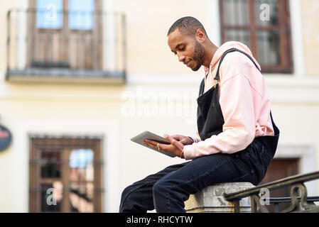 Junge schwarze Mann mit digitalen Tablet im städtischen Hintergrund.