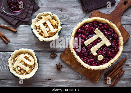 Pi-Tag Cherry und Apple Pies, hausgemachte, traditionelle verschiedene Torten mit Pi-Zeichen für 14. März Urlaub, auf hölzernen Hintergrund, Ansicht von oben. Stockfoto