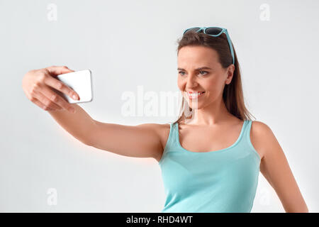 Reife Frau Sonnenbrille tragen auf dem Kopf stehend Studio isoliert auf weiße Wand unter selfie Foto auf dem Smartphone lächelt glücklich Stockfoto