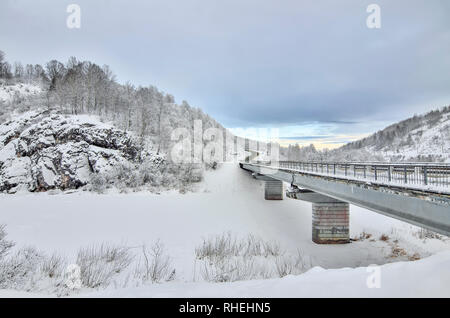 Autobahn mit Brücke durch die verschneite Felsen im Gebirge, schöne Winter twilight Landschaft. Birke und Kiefer Wald an den Hängen der Hügel mit Hoa