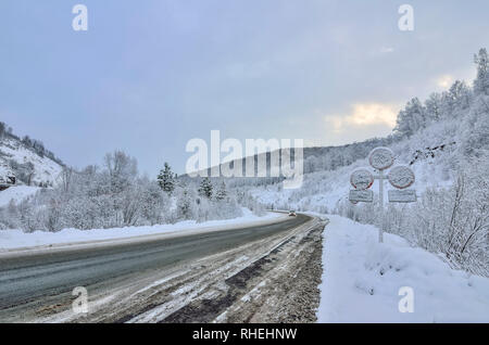 Winter wicklung Snowy Mountain Highway durch eine Berglandschaft. Abenddämmerung, Straßenschilder mit Schnee bedeckt nach einem Schneefall - die con Stockfoto