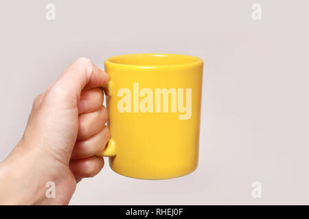 Hand, die eine gelbe Tasse auf beigem Hintergrund isoliert Stockfoto