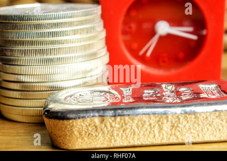 Nahaufnahme von Silbermünzen amerikanischen eine Unze Adler und Ziegel Festlegung auf hölzernen Hintergrund mit roten Uhr in der Rückseite Stockfoto