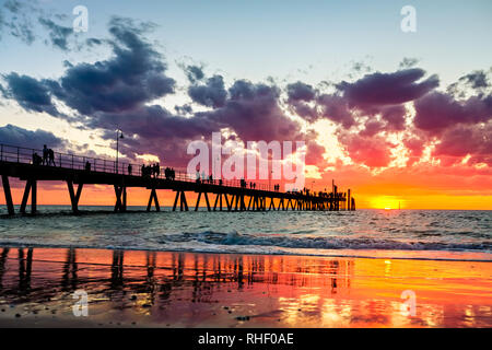 Iconic Glenelg Bootsanleger mit Menschen Silhouetten in feuchten Sand reflektiert während Bunte dramatischer Sonnenuntergang Stockfoto