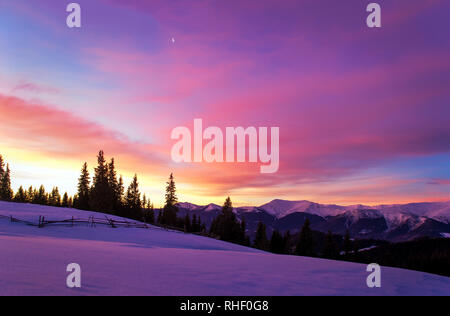 Wintermorgen Landschaft. Die Sonne geht hinter Bäumen und leuchtet die Wolken. Bergrücken. Der Mond am Himmel. Holzzaun in schneebedeckten Feld. Twili Stockfoto