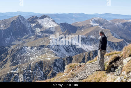 Einsamer Mann steht auf einem Berg und schaut in die Ferne auf dem Hintergrund einer Bergkette. Fokus auf den ersten Plan, auf den Mann. Berge Stockfoto