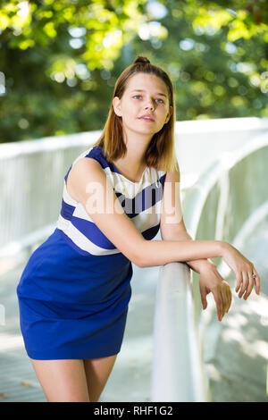 Junge Mädchen in blauem Kleid stehen auf Stadt Brücke umgeben von Bäumen Stockfoto