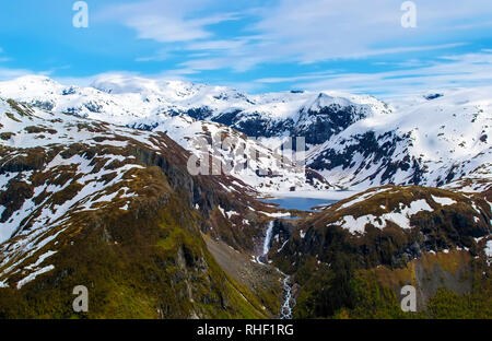 Fernsicht auf den See, von dem ein Wasserfall, zwischen schneebedeckten Bergkette, mit steilen Hängen. Feder. Schnee schmilzt. Blue Sky. National Pa Stockfoto