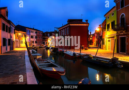 Ruhiger Abend Stadtbild von Insel Burano in Venedig. Regenbogen Farben von kleinen Hütten. Dark Blue Sky. Kleine Boote sind neben dem Wasser Kanal geparkt. Stockfoto