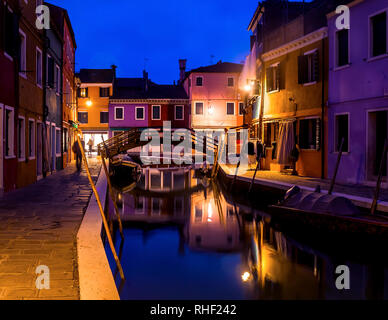 Abend Stadtbild von Insel Burano in Venedig. Farbige Gebäude und eine kleine Brücke von Straßenlaternen beleuchtet, in einem Wasserkanal wider. Stockfoto