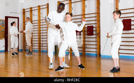 Sorgfältige ernste positive jungen Fechter aufmerksam zuhören, um professionelle Effiziente fechten Trainer im Fitnessstudio konzentriert Stockfoto