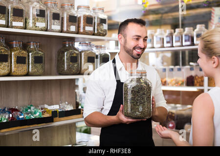 Junger Mann Verkäufer halten kann Glas mit getrockneten Kräutern in organischen Shop Stockfoto