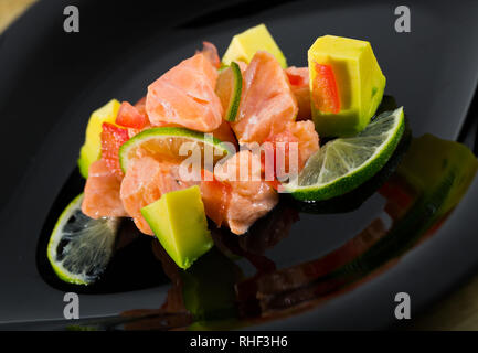 Schwarze Platte mit lecker ceviche Lachs mit Avocado und Kalk Stockfoto