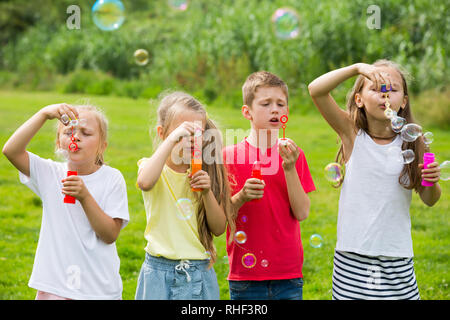 Fröhlichen Jungen und Mädchen im Grundschulalter stehen auf grünem Gras und Seifenblasen Stockfoto