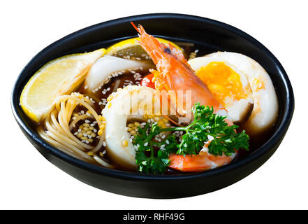 Würzige pan-asiatische Suppe gekocht mit Tintenfisch, Garnelen, eiernudeln und Sesam. Auf weissem Hintergrund Stockfoto