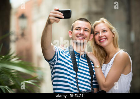Junger Mann mit Handy in der Hand und unter Selbstportrait mit Freundin in der Stadt Stockfoto