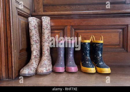 Drei Paar Gummistiefel - einen Erwachsenen und zwei Kinder - in eine Veranda eines Hauses Stockfoto