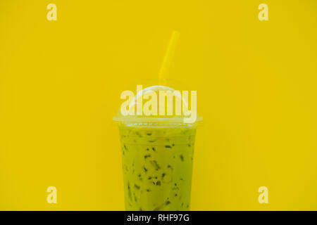 Grüner Tee Latte mit Eis in Plastikbecher und Stroh in weiblicher Hand mit gelben Maniküre auf gelben Hintergrund. Hausgemachte Eistee Matcha Latte Tee mit Milch Stockfoto