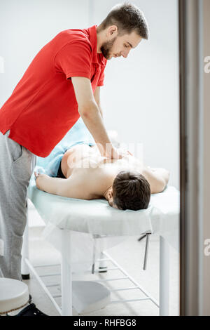Junge männliche Therapeuten, Rückenmassage, die einem Mann im weißen Schrank der Rehabilitationsklinik liegen Stockfoto