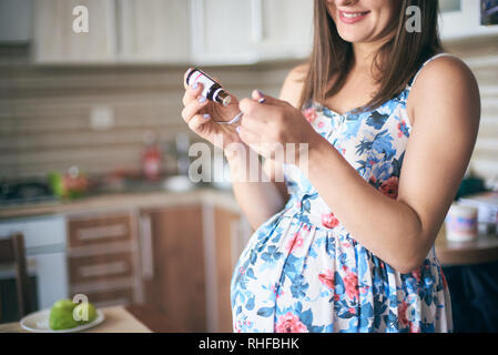 7/8-Ansicht von Medizin in den Händen von lächelnden schwangere Frau steht in der Küche. Junge zukünftige Mutter erwartet kleines Baby und Vitamine für die Gesundheit. Konzept der Pflege und der Schwangerschaft. Stockfoto