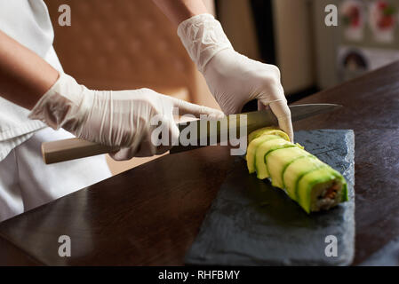 Detailansicht des Prozesses der Vorbereitung Rolling Sushi. Koch ist die Rolle auf den schwarzen Stein Platte Stockfoto