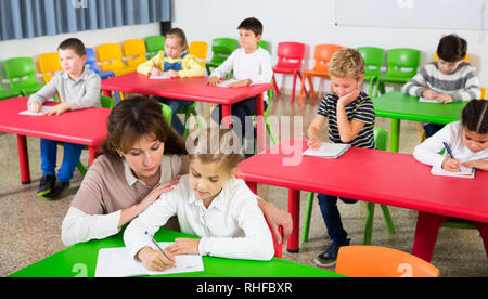 Freundliche Lehrerin Frau Kinder helfen Kindern während der Lektion im Schulzimmer Stockfoto