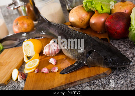 Ganz frischen Stör liegen auf Holz Schneidebrett mit Gemüse und Gewürzen auf Stein Tischplatte Stockfoto