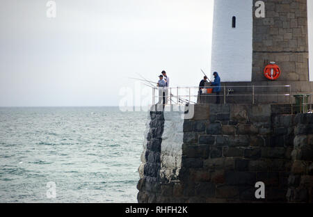 Vier Männer/jungen Fischen aus dem Leuchtturm am Ende der Hafenmauer in St Peter Port, Guernsey, Channel Islands.de. Stockfoto