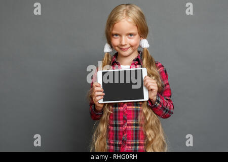 Mädchen mit zwei pferdeschwänze Studio stehen isoliert auf graue Wand angezeigt Bildschirm digitaler Tablet suchen Kamera lächelnd verspielt Stockfoto