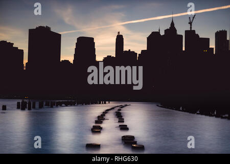 Silhouette der Skyline von Lower Manhattan bei Sonnenuntergang vom Brooklyn Bridge Park, Brooklyn, New York, USA Stockfoto