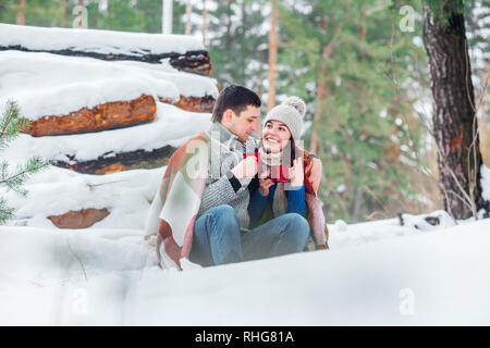 Lächelnden jungen Paar mit cups im Snow park sitzen. Trinken Sie heiße Getränke, Spaß zu haben. Stockfoto
