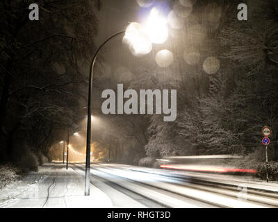 Verschneite Straße mit street Lichter in der Nacht, Auto mit Motion Blur das Fahren auf einer schneebedeckten Straße mit street Lichter in der Nacht, Schneefall Stockfoto