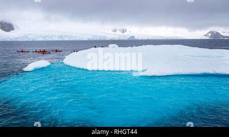 Riesiger Eisberg mit blauen Unterwasser teil und kleinen Touristen Kajaks mit Antarktis Lagune im Hintergrund, Peterman Island, Antarktische Halbinsel Stockfoto