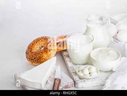 Frische Milchprodukte in Vintage hölzerne Kiste auf weißem Hintergrund. Glas und Glas Milch, Schüssel mit saurer Sahne und Käse. Frisch gebackene Bagels. Stockfoto