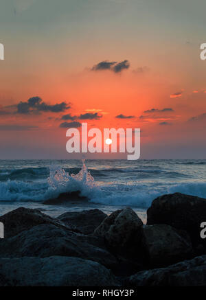 Kleine Wave splash auf einem felsigen Ufer Strand bei Sonnenuntergang mit warmen Farben des Sommers, Wassertropfen fliegen in der Luft. Stockfoto