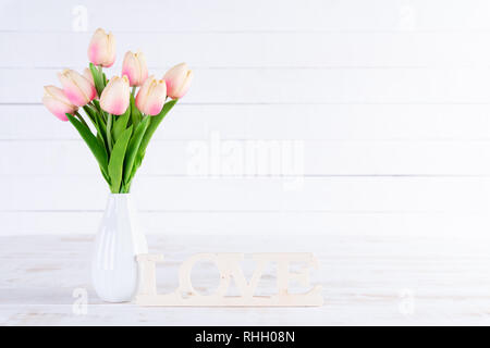 Valentines Tag und liebe Konzept. Rosa Tulpen in der Vase mit Holz Buchstaben bilden Wort LIEBE auf weißem Holz- Hintergrund geschrieben. Stockfoto