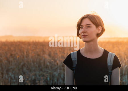 Hintergrundbeleuchtung Porträt einer Frau, die in den Sonnenuntergang. Weibliche Person, die in der Abendsonne in ein Feld Stockfoto