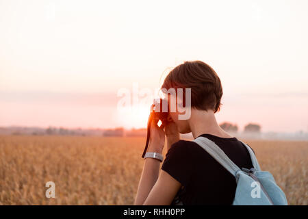 Hintergrundbeleuchtung Abbildung einer Frau ein Foto im hellen Sonnenuntergang. Weibliche Person, die in der Abendsonne in ein Feld und mit alten analogen Kamera Stockfoto