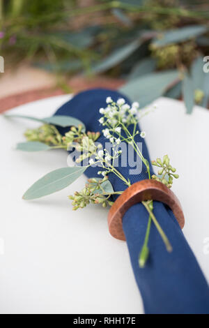 Blau serviette in Ring auf weiße Platte mit Kupfer Ladegerät, setzen Sie die Einstellung auf Holz Outdoor Party Esstisch mit Blumen. Stockfoto