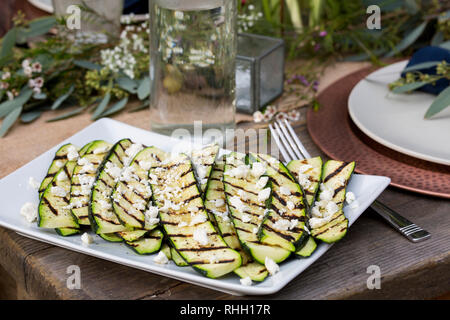Weiße rechteckige Servierplatte von gegrillten Zucchini auf hölzernen Tisch für Mahlzeiten im Freien Hinterhof Dinner Party. Stockfoto