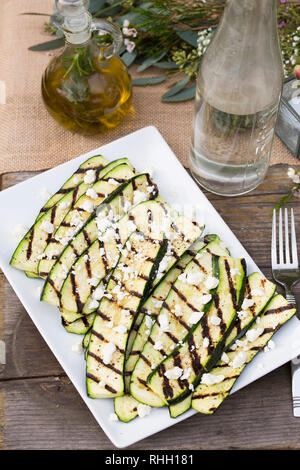 Weiße rechteckige Servierplatte von gegrillten Zucchini auf hölzernen Tisch für Mahlzeiten im Freien Hinterhof Dinner Party. Stockfoto