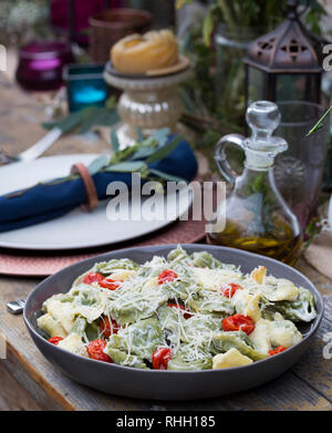 Servierschale von Grün und Gelb Ravioli mit Tomaten und geriebenem Parmesan auf hölzernen Tisch für Hinterhof outdoor Dinner Party, mit Olivenöl. Stockfoto